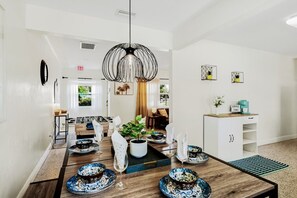 Un espace repas moderne avec une table en bois dressée pour le repas, un luminaire suspendu et une vue sur le salon.