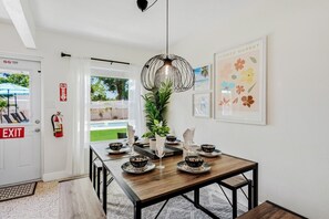 Un coin repas avec une table en bois, des chaises noires, un luminaire suspendu et un extincteur fixé au mur.