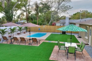 A backyard with a swimming pool, patio furniture, and a well-maintained lawn.