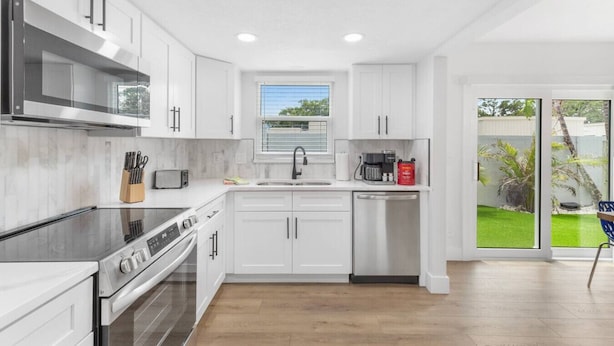 A modern kitchen with white cabinets, stainless steel appliances, and a window with a view of greenery. - Chic Coastal Getaway (Largo)