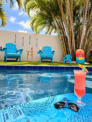 Une piscine avec des chaises bleues et un cocktail exotique.