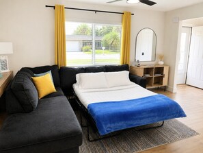 Een slaapkamer met een bed, een slaapbank, een nachtkastje, een spiegel en een raam met gordijnen.