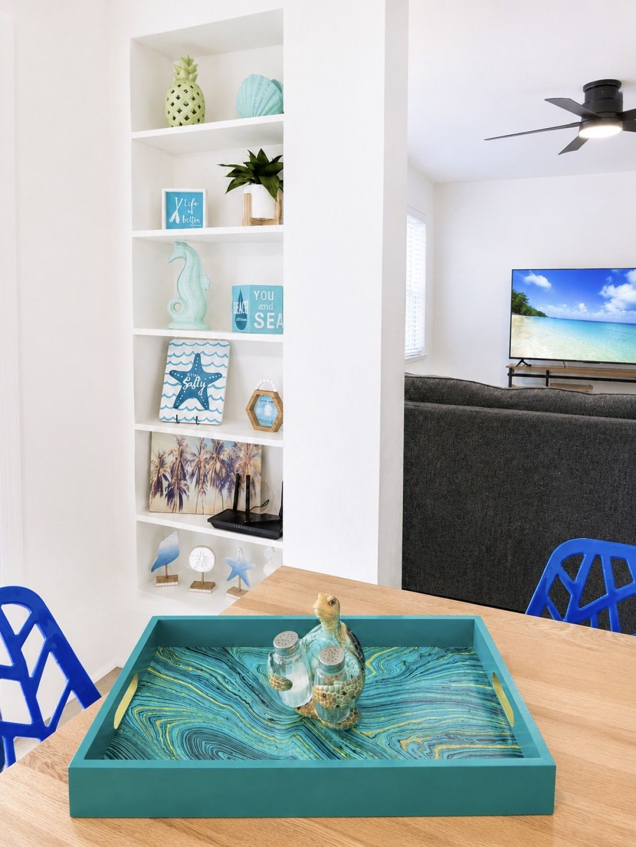 Ein Zimmer mit weißer Wand, einem Regal mit Dekoration, einem Fernseher und einem Tisch mit Tablett.