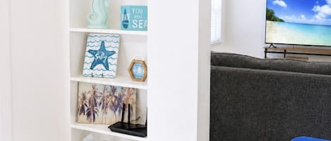 Ein Zimmer mit weißer Wand, einem Regal mit Dekoration, einem Fernseher und einem Tisch mit Tablett.