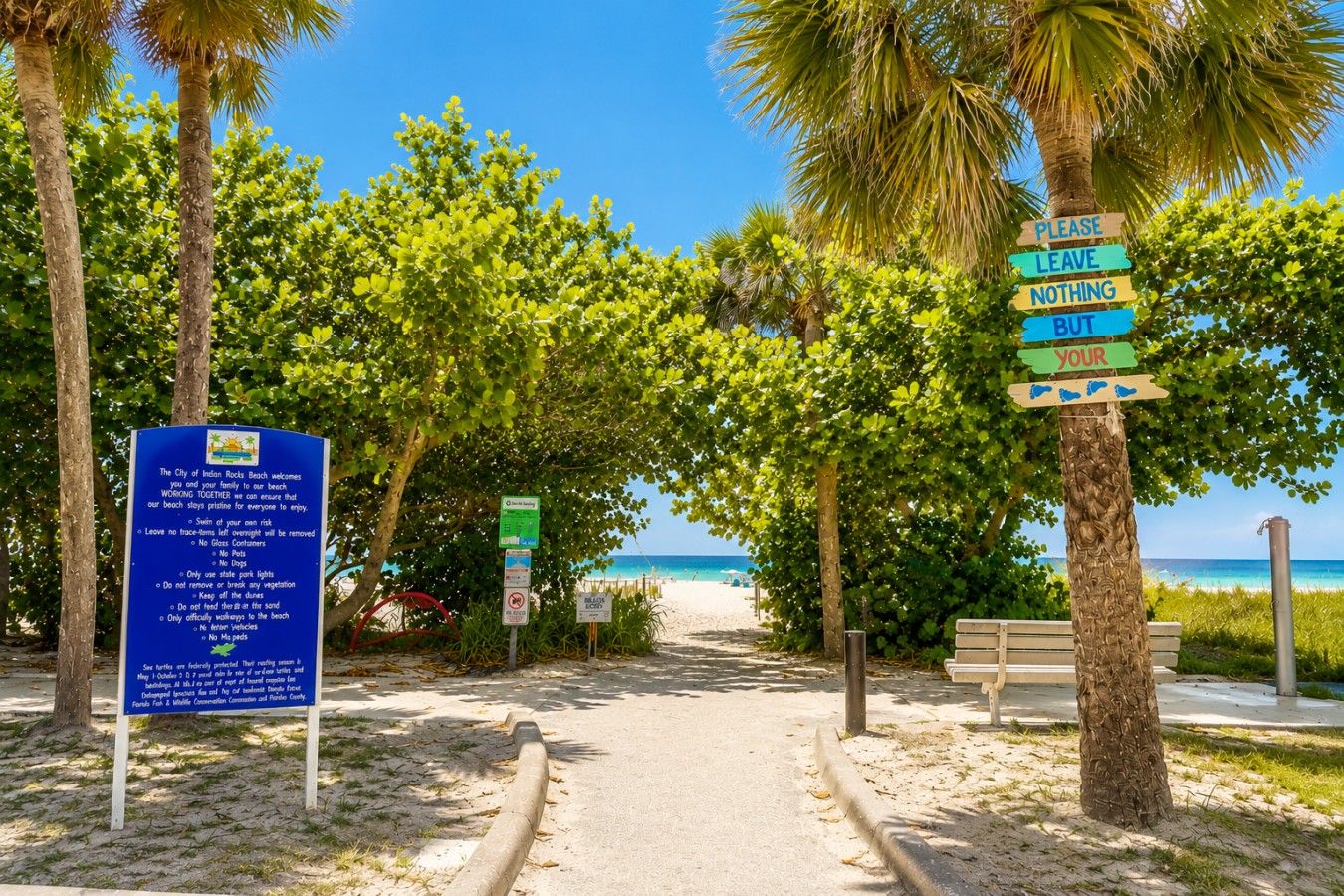 A pathway leading to a beach with palm trees and a sign that says 'PLEASE LEAVE NOTHING BUT YOUR'.