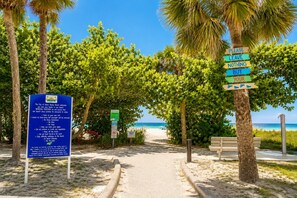 Un sentier menant à une plage bordée de palmiers, avec un panneau indiquant : « VEUILLEZ NE LAISSER DERRIÈRE VOUS QUE VOS PAS. »