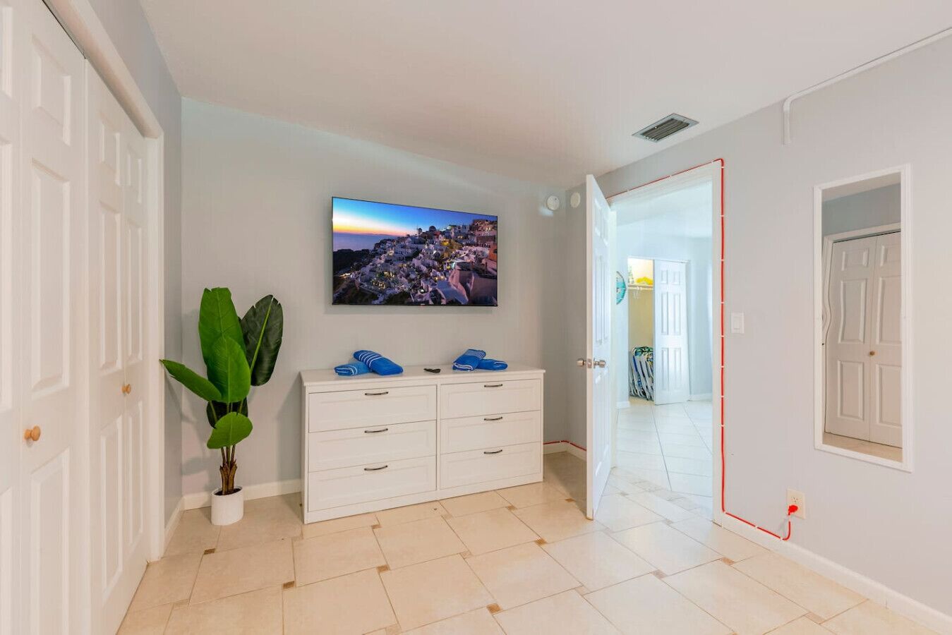 Una habitación con un aparador blanco, una planta en maceta, un televisor de pantalla plana en la pared y un pasillo que conduce a otra habitación.