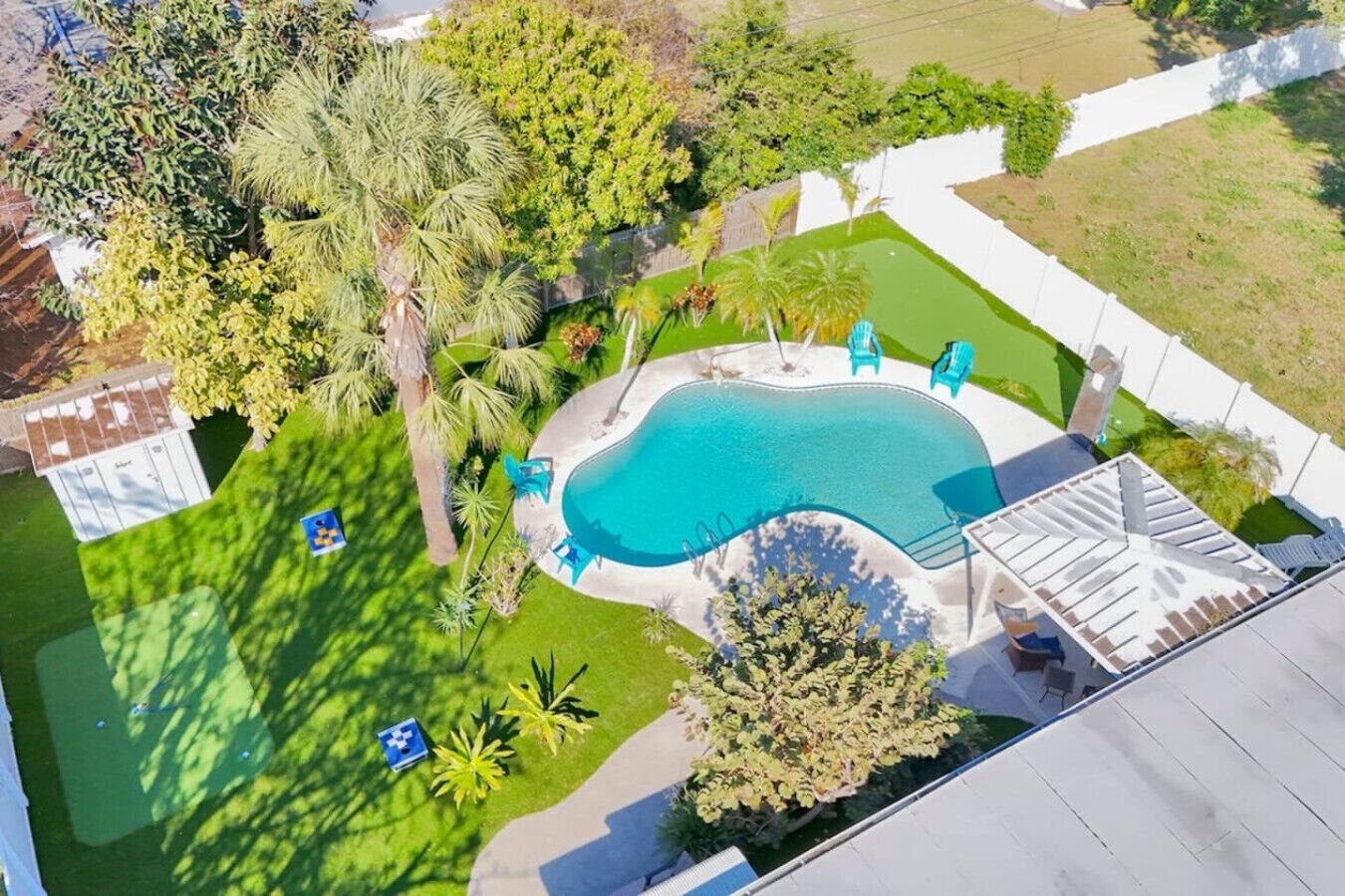 Vista aérea de un patio trasero con piscina, rodeado de palmeras y césped.