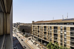 Ein mehrgeschossiges Gebäude mit einer rasterartigen Fassade, eine Straße mit Fahrzeugen und ein klarer Himmel.