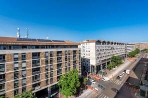Ein mehrstöckiges Gebäude mit modernem architektonischen Design, das Backstein- und Glasfassaden kombiniert und eine Dachterrasse mit Solaranlagen aufweist.