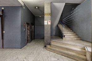 Una escalera que conduce a un piso superior, una puerta con manija de metal y un cartel que dice 'Scala B'.