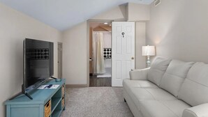 A modern living room with a flat-screen TV, a light-colored sofa, and a teal console table. - Charming 1-bedroom house in fabulous Florence Alabama (Florence)
