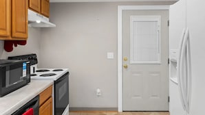 A compact kitchen with a stove, microwave, and oven, wooden cabinets, and a white door with a window. - Charming 1-bedroom house in fabulous Florence Alabama (Florence)