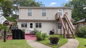 A two-story house with a red front door, a covered patio with outdoor furniture, and a large planter in the front yard. - Charming 1-bedroom house in fabulous Florence Alabama (Florence)