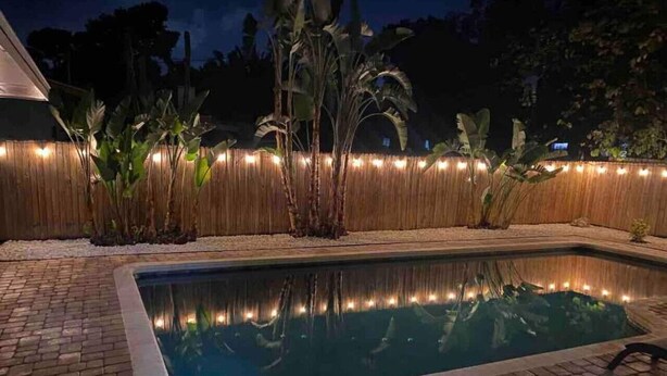 A swimming pool with a brick border, surrounded by a wooden fence and plants. - Villa Bella with Heated Pool (Largo)