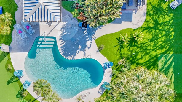 An aerial view of a swimming pool with lounge chairs and a covered area with a striped roof.