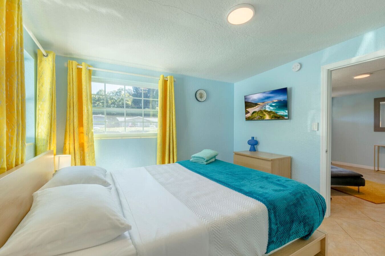 A bedroom with a bed, a nightstand, a lamp, a clock, and a painting on the wall.