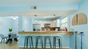 A modern kitchen with a central island, bar stools, and a dining area with a table and chairs.