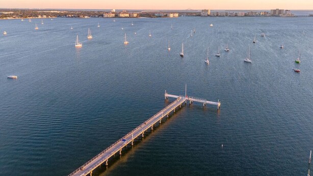 An aerial view of a marina with numerous sailboats and a long pier extending into the water.