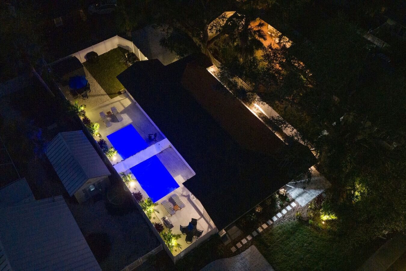 An aerial view of a residential property with a swimming pool, outdoor seating area, and a well-lit garden.