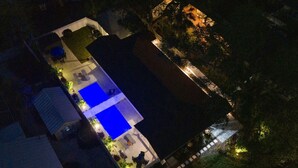 An aerial view of a residential property with a swimming pool, outdoor seating area, and a well-lit garden.