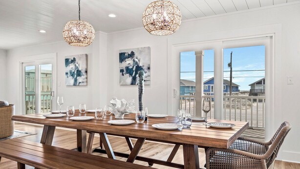 A dining area with a wooden table set for six, two hanging wicker chandeliers, and artwork on the walls. - NEW - Ocean View, Heated Pool, Beach, Sleeps 18, Fully Loaded (Gulf Shores)