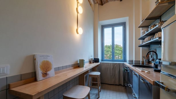 A kitchen with a wooden countertop, stools, a window, and a view of greenery outside. - GuestHost - Elegant Apartment Testaccio Roma (Rome)