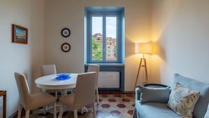A room with a dining table, chairs, a blue-framed window, a standing lamp, and a sofa. - GuestHost - Elegant Apartment Testaccio Roma (Rome)