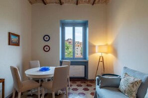 Una habitación con una mesa de comedor, sillas, un ventanal con marco azul, una lámpara de pie y un sofá.