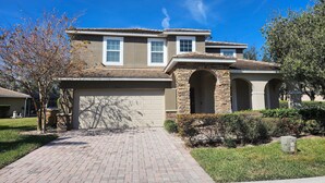 A two-story house with a brick driveway, a garage, and a stone archway.