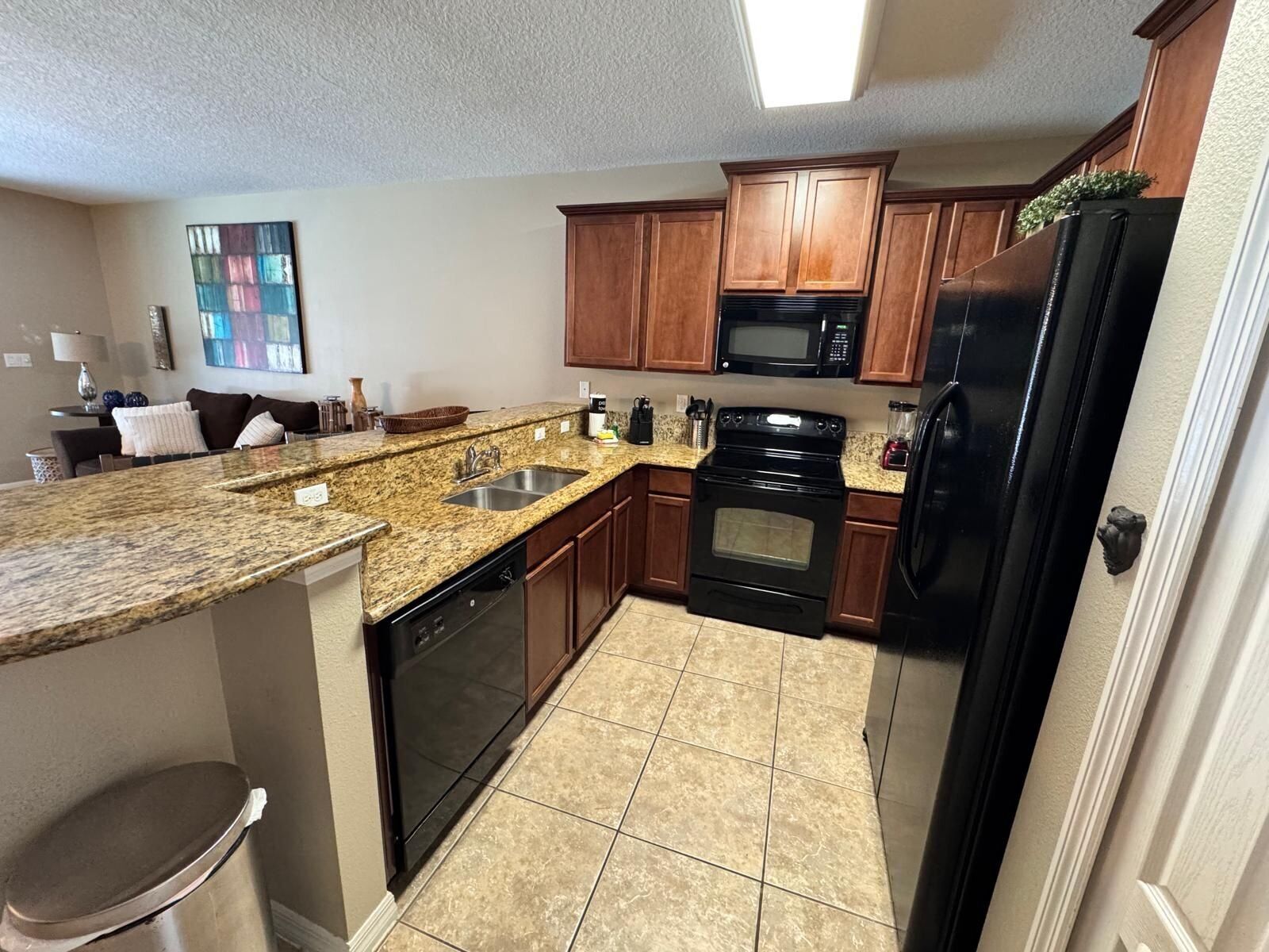 A compact kitchen with granite countertops, wooden cabinets, a black refrigerator, a microwave, and a dishwasher.