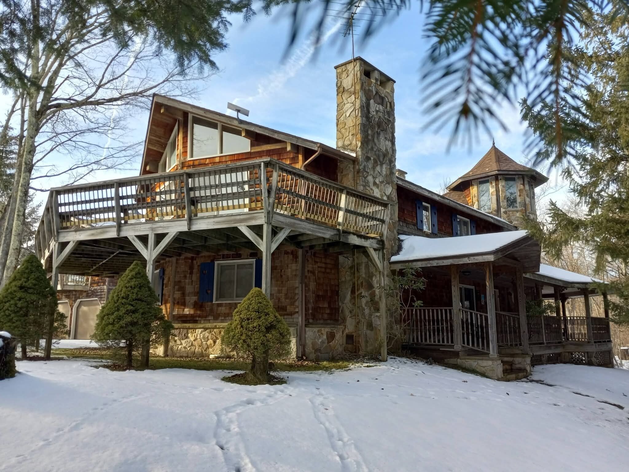 A cabin with a stone chimney, wooden deck, and a stone tower.