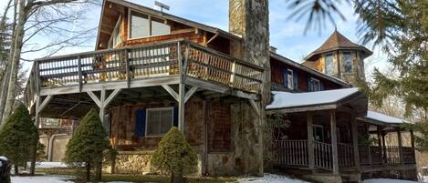 A cabin with a stone chimney, wooden deck, and a stone tower.