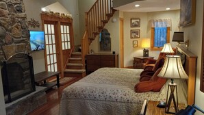 A cozy bedroom with a stone fireplace, a wooden staircase, a bed with a floral bedspread, and a nightstand with a lamp. - The Golden Eagle Vacation Rental, a 3 minute walk to Timberline Ski Slopes (Davis)