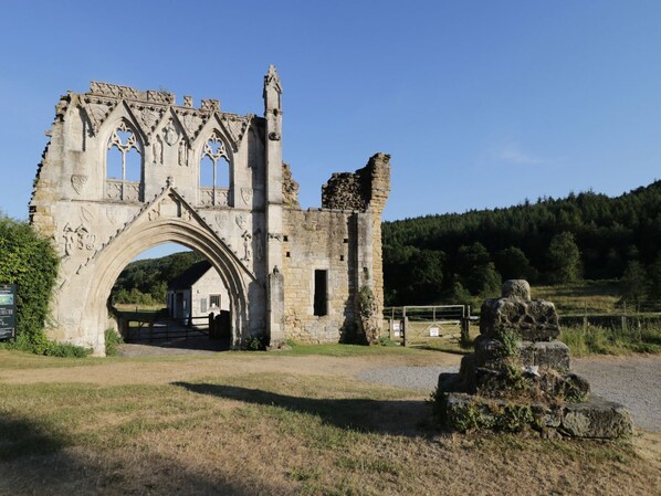 A historic stone archway leading to a building with a gabled roof, surrounded by a rural landscape.