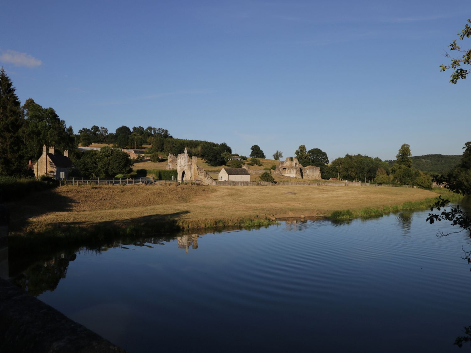 Una vista tranquilla lungo il fiume, con edifici storici in pietra, un ponte e una superficie d'acqua calma che riflette le costruzioni.