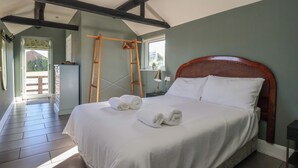 Un lit bien fait, avec du linge de lit et des serviettes blanches, une échelle en bois et une tête de lit en bois, dans une pièce aux murs verts et au plafond en pente.