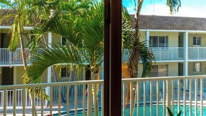 A hotel with a pool, multiple balconies, and palm trees. - Nautilus 214 by Nautilus Vacations-Beachfront Complex, Heated Pool, Racket Court (Holmes Beach)