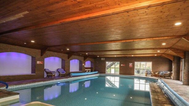 En indendørs swimmingpool med træloft, flisegulv og liggestole.