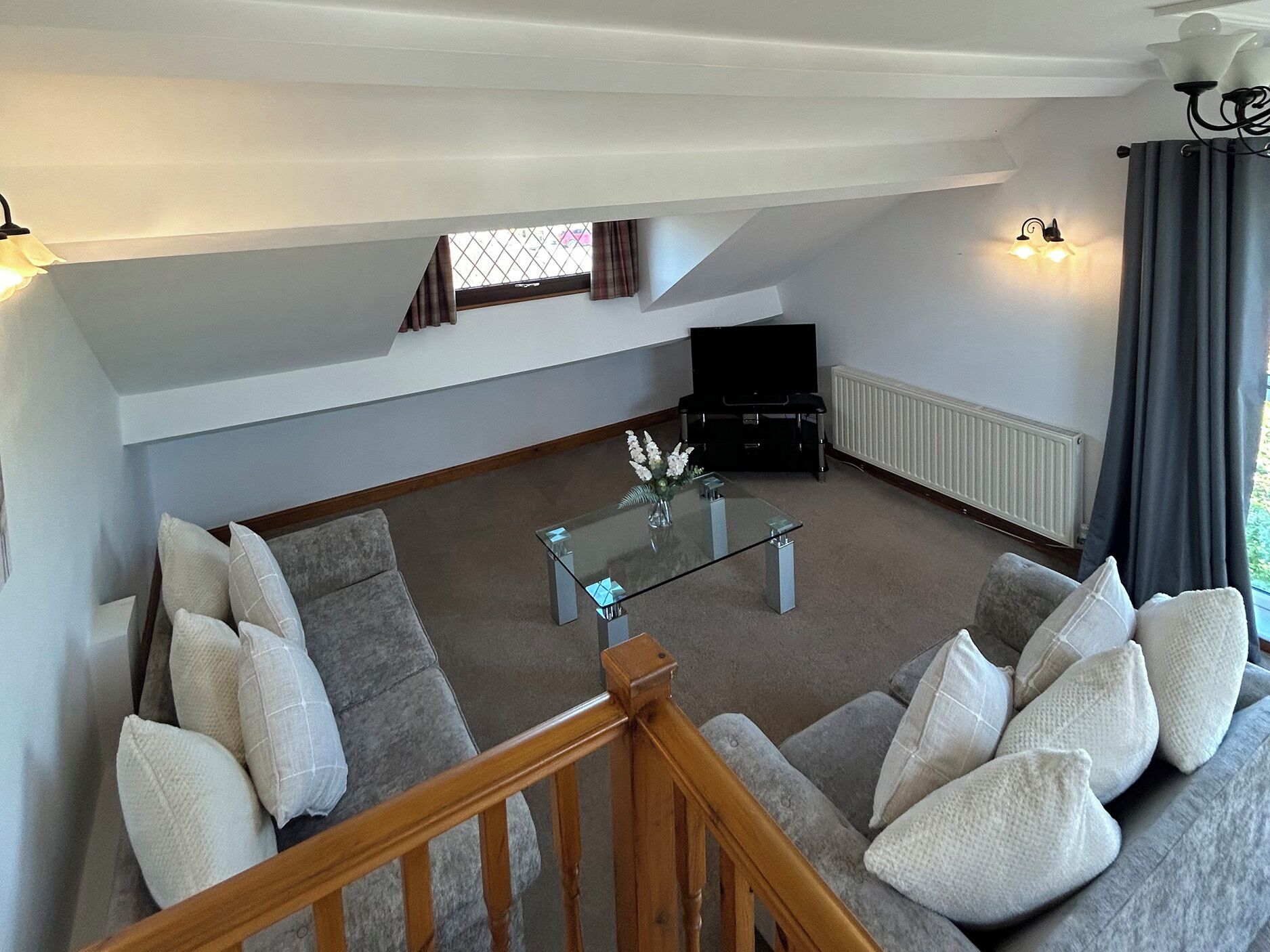 A living room with a sofa, a glass coffee table, a flat-screen TV, and a staircase.