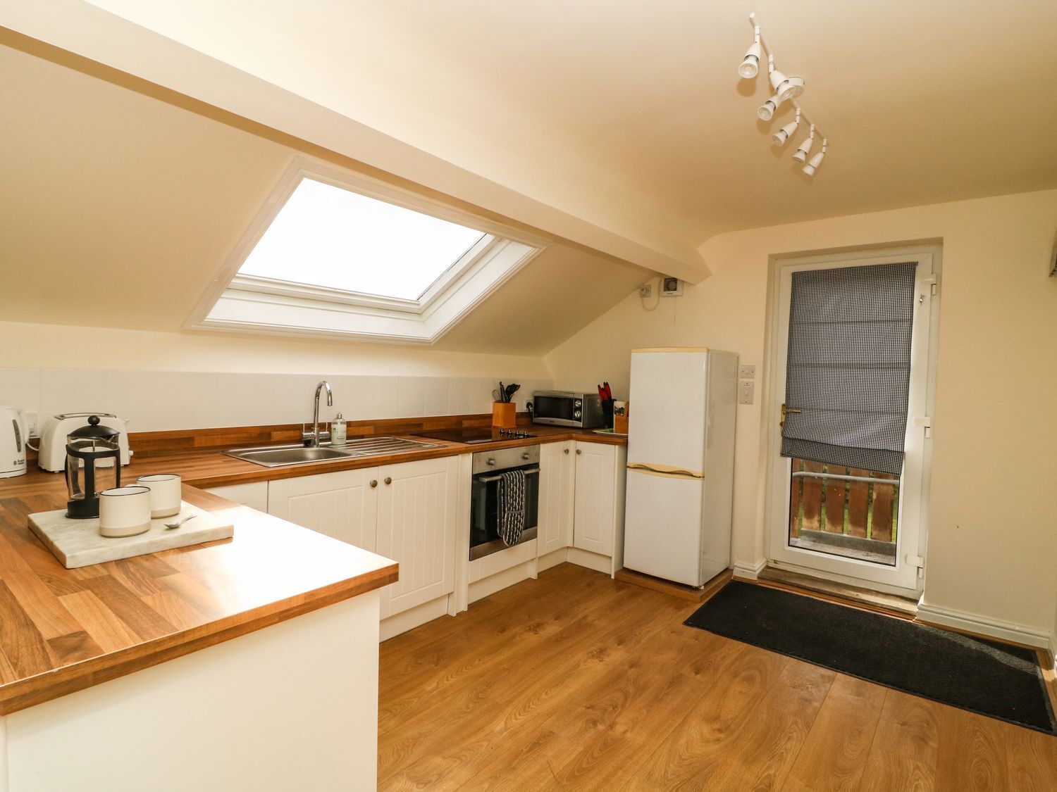 A compact kitchen with a skylight, wooden countertop, white cabinets, a built-in oven, and a refrigerator.