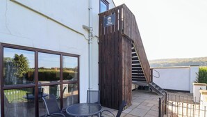 A patio with a table and chairs, a wooden staircase, and a sign for 'West Cottage'. - West Cottage (Malton)