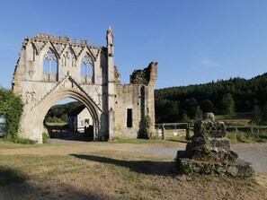 Un arc en pierre d’époque mène à un bâtiment doté d’un toit à pignon, le tout étant situé au cœur d’un paysage rural.