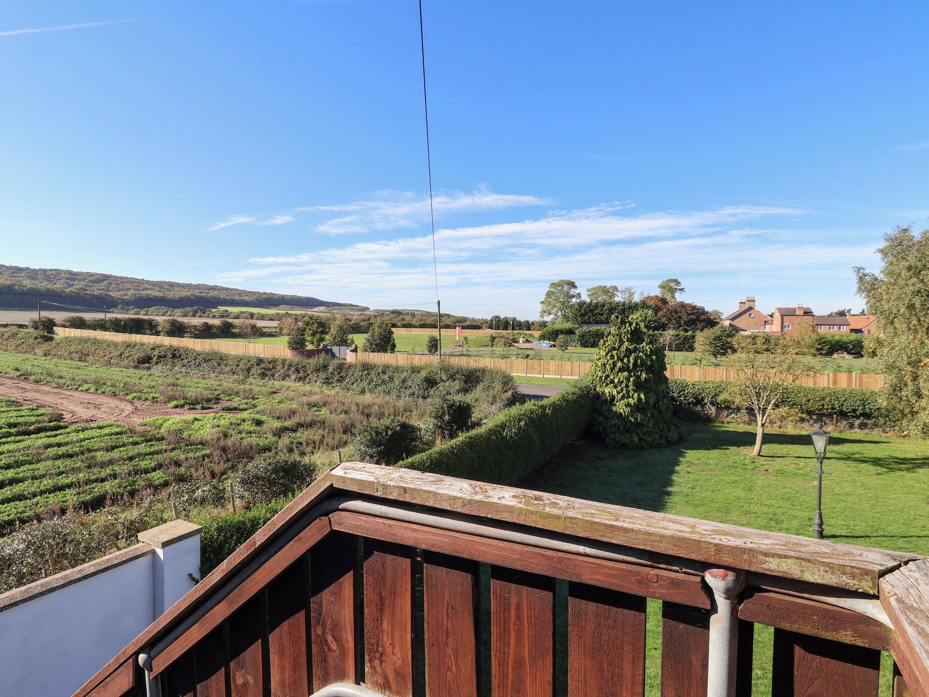 Zona residencial com deck de madeira, vista para um campo verde e uma colina ao longe.