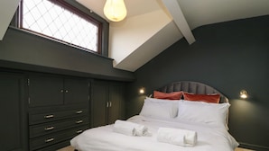 A bedroom with a large bed, dark walls, a window, and built-in wardrobe. - West Cottage (Malton)