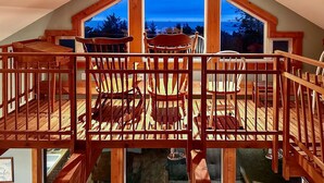 Une terrasse en bois avec une table et des chaises, une balustrade en bois et une grande fenêtre donnant sur un paysage.