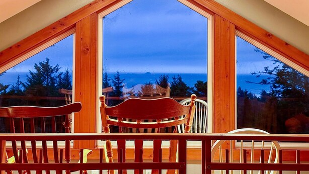 Une pièce dotée d’une grande fenêtre triangulaire qui offre une vue sur l’extérieur. On y trouve des chaises et une table en bois.
