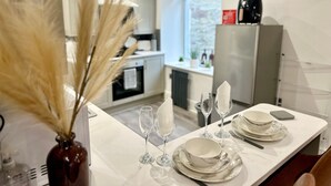 Una cucina moderna con mobili bianchi, un frigorifero e un'area pranzo apparecchiata con piatti, ciotole e bicchieri da vino bianchi.