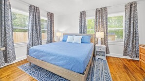 Une chambre à coucher avec un lit en bois, des rideaux à motifs, une table de chevet et une fenêtre avec des stores.