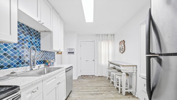 Une cuisine moderne avec des meubles blancs, un réfrigérateur en acier inoxydable et un dosseret de carrelage bleu.